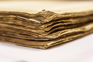 Makro zbliżenie na róg starej, pożółkłej księgi lub stosu archiwalnych dokumentów. Widoczne tekstury zniszczonego papieru i warstwy historii. Antyczny, vintage styl na białym tle.