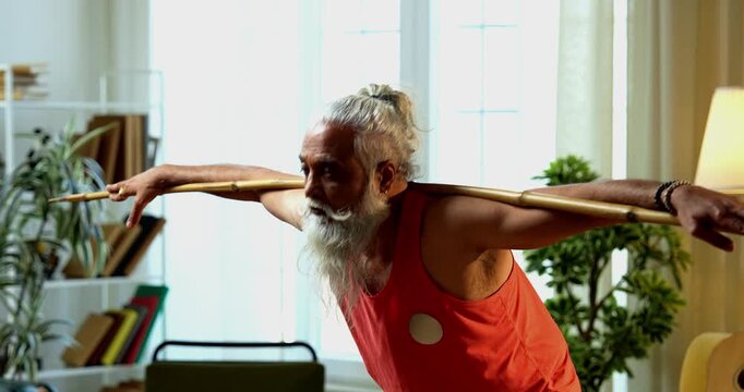 Indian mid age stylish bearded man doing exercise using stick, rod or staff at home, fitness conscious mature male performing strength and mobility workout showing agility and determination