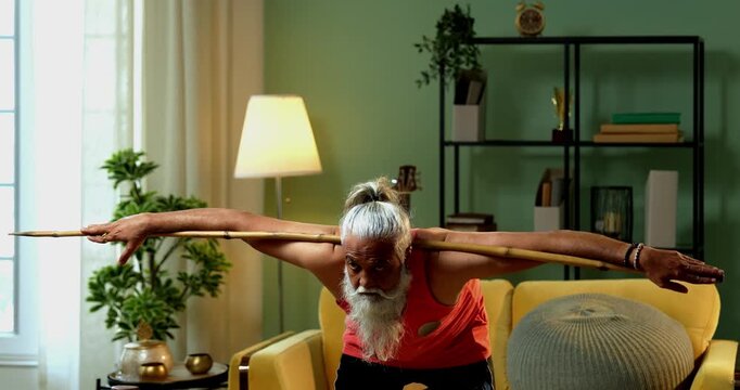 Indian mid age stylish bearded man doing exercise using stick, rod or staff at home, fitness conscious mature male performing strength and mobility workout showing agility and determination
