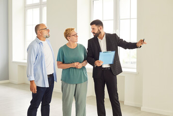 Realtor and agent guide a senior couple through new apartment during a tour and viewing, helping buyers assess the interior and showing key home features. Real estate market and buying property.