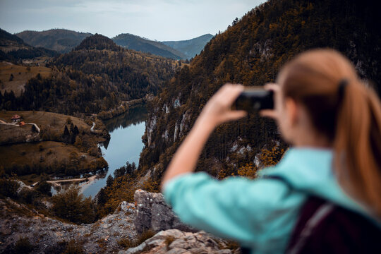 Woman photographing river valley from mountain viewpoint