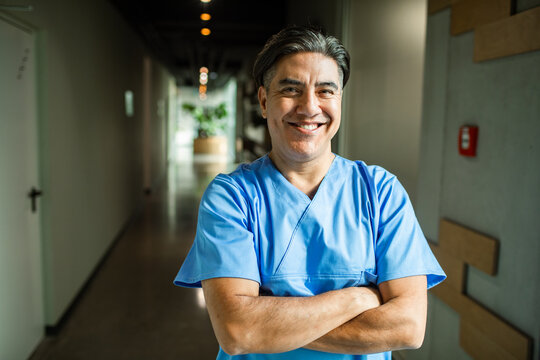 Smiling male nurse with crossed arms in hospital corridor