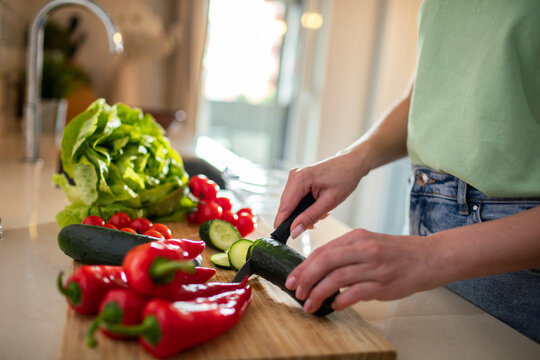 Woman slicing cucumber on cutting board in home kitchen