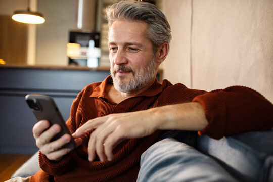 Middle-aged man using smartphone on home sofa