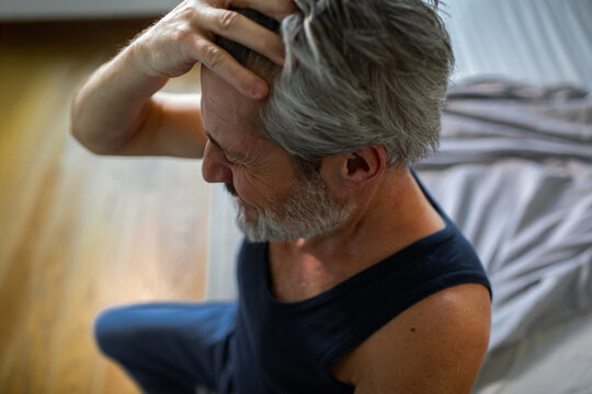 Mature man with headache sitting on bed at home