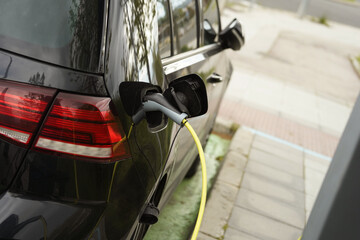 Un coche eléctrico con el enchufe y el cable conectados para cargar la batería en un espacio de estacionamiento en la calle. © Oscar Martín