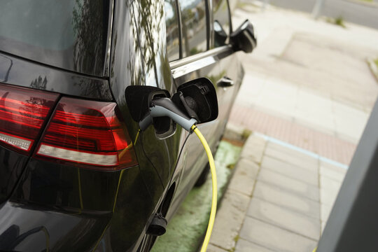 Un coche el&eacute;ctrico con el enchufe y el cable conectados para cargar la bater&iacute;a en un espacio de estacionamiento en la calle.