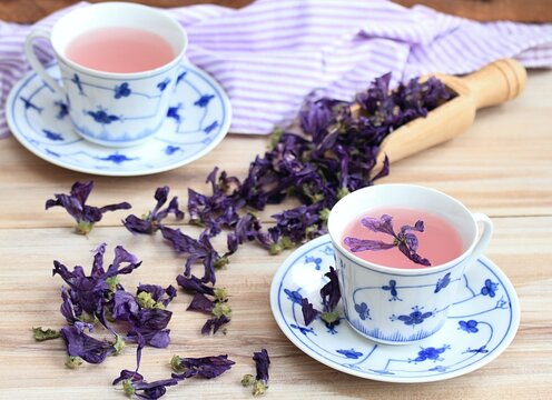 Two cups of herbal tea from dried flowers of Wild mallow, lat.  Malva sylvestris. Traditional curative herbal tea against cough.  Dried flowers in a spoon and around.