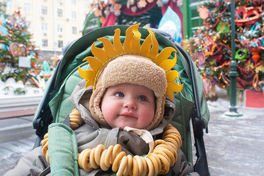 baby boy in sun hat and ushanka with sushki necklace at maslenitsa festival in moscow

