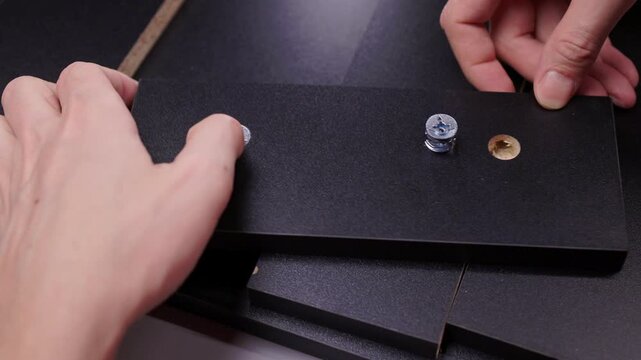 Hands assembling flat pack furniture, connecting wood panels with screws, cam locks and dowels, creating structure during home improvement project, close-up, slow motion.
