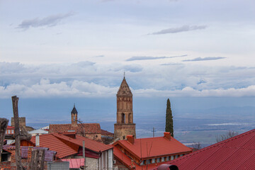 Rooftops of the old town. A church bell tower. The Alazani Valley, the Caucasus Range, and snow-capped mountains in the background. St. Tamar the Queen basilica, Sighnaghi, Kakheti, Georgia