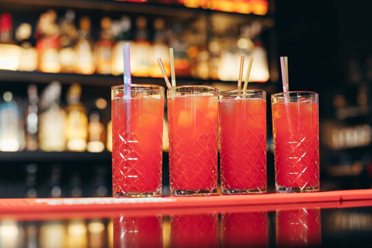 Four Red Cocktails With Straws On Bar