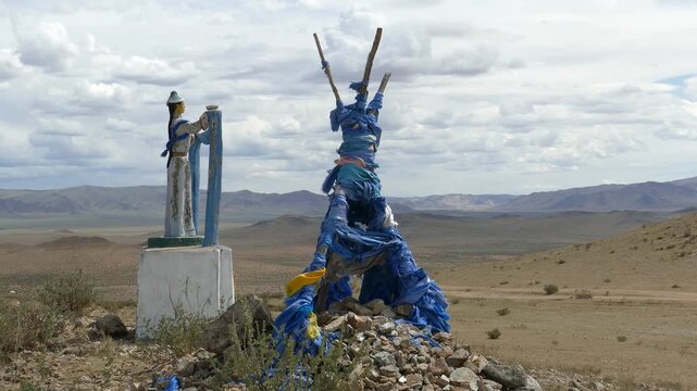 Santmargats, MONGOLIA - July 18, 2017. Ritual pile of stones (ovoo, oboo) and sculpture women c with a scarf in their hands against the backdrop of a picturesque cloudy sky and mountains in the distan