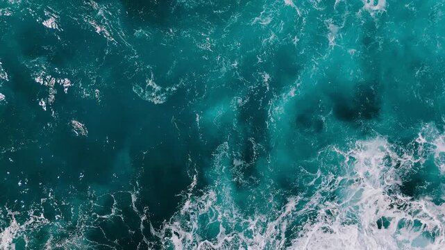 Powerful sea surface seen from above, waves breaking and mixing in deep blue water.