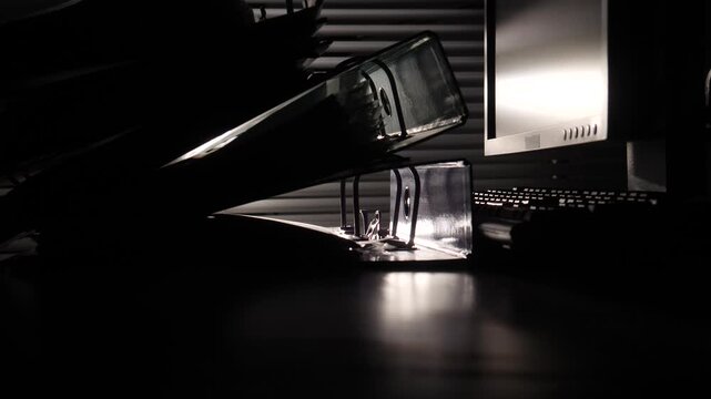 Office binders and computer monitor in silhouette against a dark background, representing concepts of bureaucracy, hidden work, and stressful overtime during late hours