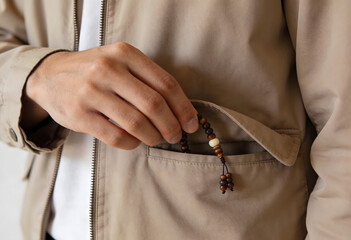 Person discreetly putting prayer beads into coat pocket, close-up shot