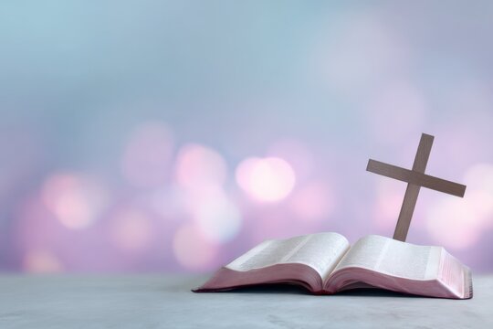 Open bible with small wooden cross on a table with soft pastel bokeh background spiritual faith concept