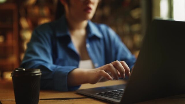 Young Asian woman typing on laptop in library, fixing computer program error