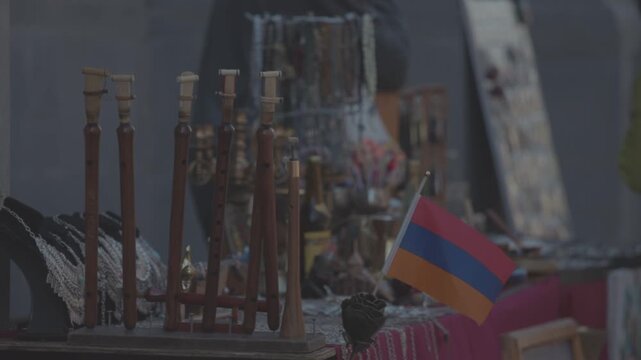 Traditional Armenian woodwind musical instruments, known as duduks, are beautifully displayed for sale at an outdoor souvenir market stall, standing next to a small national flag of Armenia.

