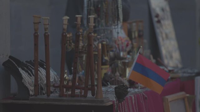 Traditional Armenian woodwind musical instruments, known as duduks, are beautifully displayed for sale at an outdoor souvenir market stall, standing next to a small national flag of Armenia.

