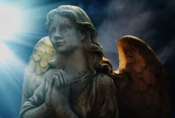 Naklejka premium Angel statue in prayer illuminated by heavenly light rays, symbol of hope, protection, spirituality, and divine presence.
