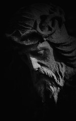 Naklejka premium Dark dramatic close-up of Jesus Christ stone statue in deep shadow, symbol of suffering, sacrifice, faith, and spiritual endurance.