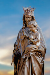 Naklejka premium Crowned Virgin Mary holding Child Jesus against soft sky, symbol of motherhood, faith, divine love, and sacred protection.