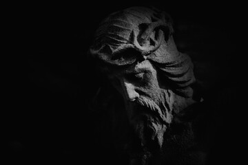 Fototapeta premium Dark dramatic close-up of Jesus Christ stone statue in deep shadow, symbol of suffering, sacrifice, faith, and spiritual endurance. Copy space for text or design.