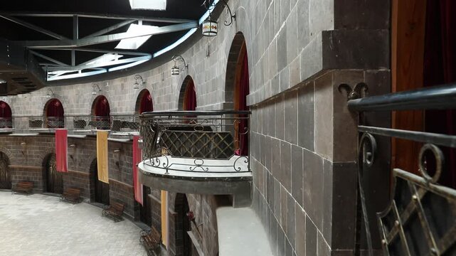 Panning shot of a large, empty circular hall with stone walls, wooden stage, red chairs, and multiple balconies decorated with red curtains. A unique, historic-looking indoor event space.

