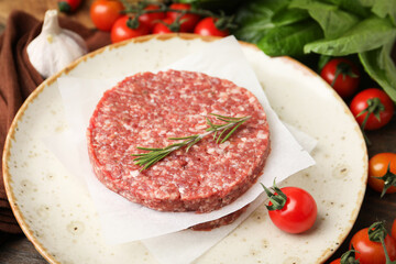 Uncooked meat patty with rosemary, tomatoes, lettuce and garlic on table, closeup
