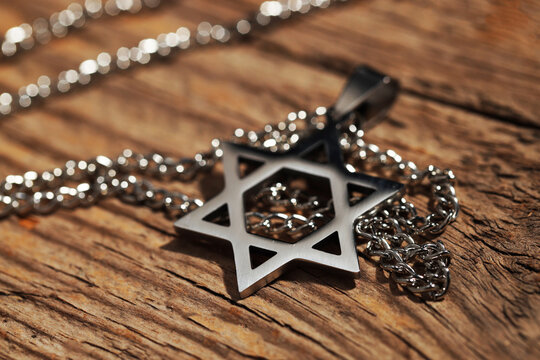 Holocaust Remembrance Day. Pendant in shape of Star of David and metal chain on wooden table, closeup
