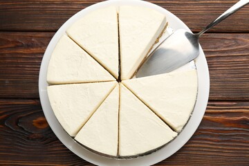 Tasty cut cheesecake and server on wooden table, top view