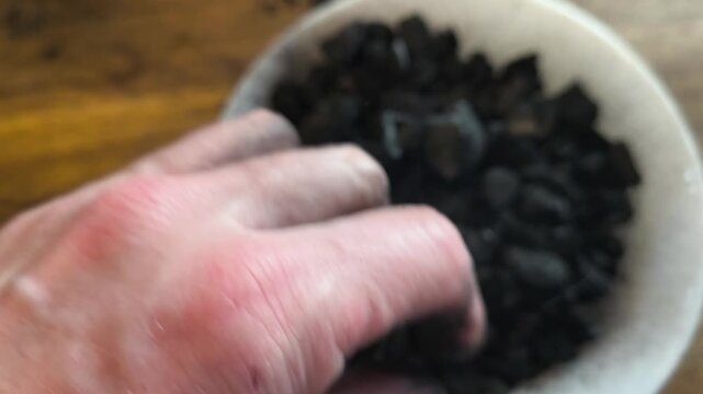 Close-up of a gardener's hands crushing natural charcoal to create biochar for a potting mix. Sustainable soil amendment and permaculture gardening techniques
