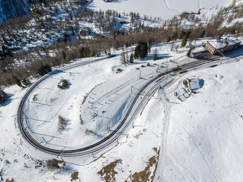 Aerial image of the Rhaetian Railway track with the famous tight 180&deg; curve at high Alp Grum over Berina Pass down into the Poschiavo Valley.