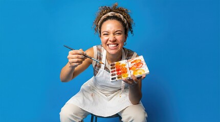 Young woman artist holding paintbrush and watercolor palette on blue background