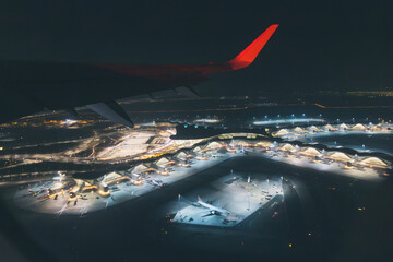 Airplane wing overlooking a vibrant modern airport terminal building and runways illuminated at night, representing global connectivity and travel