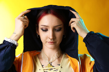 Beautiful young woman with piercings in windbreaker on yellow background © New Africa