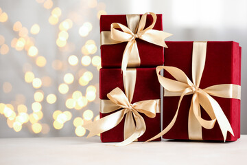 Fototapeta premium Red gift boxes on white table against blurred bokeh lights, closeup. Space for text