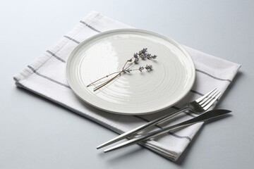 Stylish setting with cutlery, lavender flowers and napkin on light grey table, closeup