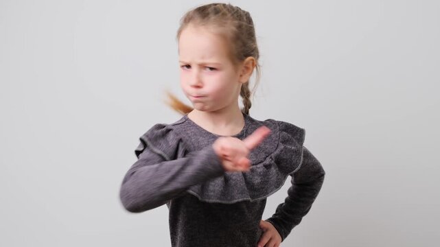 Young Girl Points Finger in Warning Gesture: Displeased Child on Gray Background, Expressing Stop or No, Dissatisfied Kid