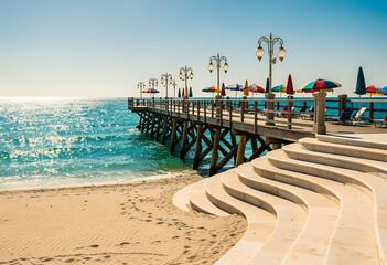 Obraz premium Beach pier on sunny seaside with umbrellas and blue water