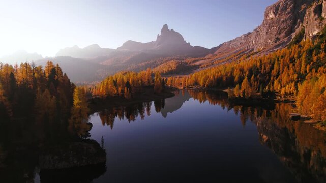 Flying above Lago Federa lake surrounded by golden larch forest in the Dolomites, Italy