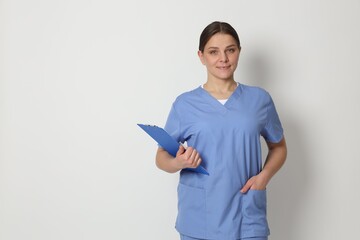 Portrait of medical worker in blue uniform with clipboard on light background. Space for text