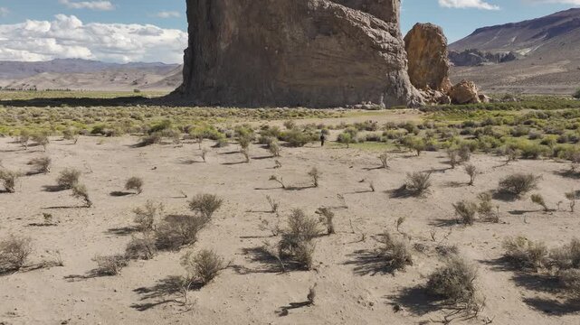 Drone shot rising in front of massive volcanic monolith known as Piedra Parada with a person walking in a desert valley. Patagonia, Argentina