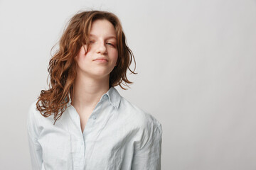 Obraz premium Young woman with curly hair wearing white shirt poses with confident expression on light background. Concept of natural beauty, casual style, and self-confidence.