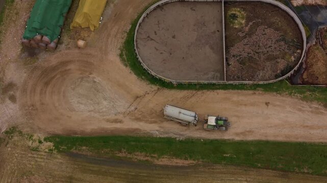 Farmyard Operations: An aerial view showcases agricultural activity, with a tractor and trailer navigating a dirt track past storage facilities and a large oval containment area.