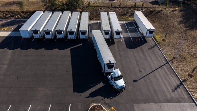 Aerial/drone views of white semi trucks with refrigerated trailers parked outside a warehouse parking lot	