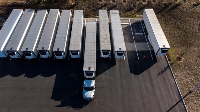Aerial/drone views of white semi trucks with refrigerated trailers parked outside a warehouse parking lot	
