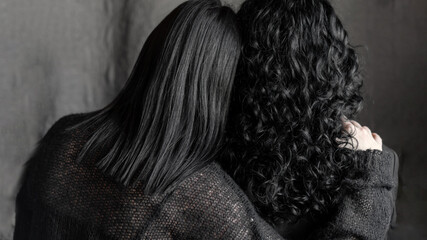 two women with black hair hugging. back view. curly and straight hair. hug, care, support, psychology. two sisters. european woman with dark black hair, romance, relationship