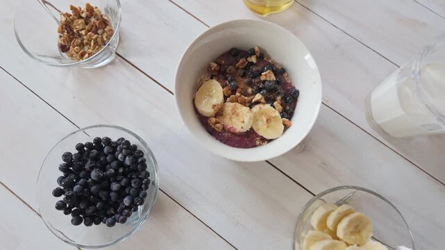 Slow motion lateral shot across oatmeal breakfast with berries, banana and honey arranged on wooden table